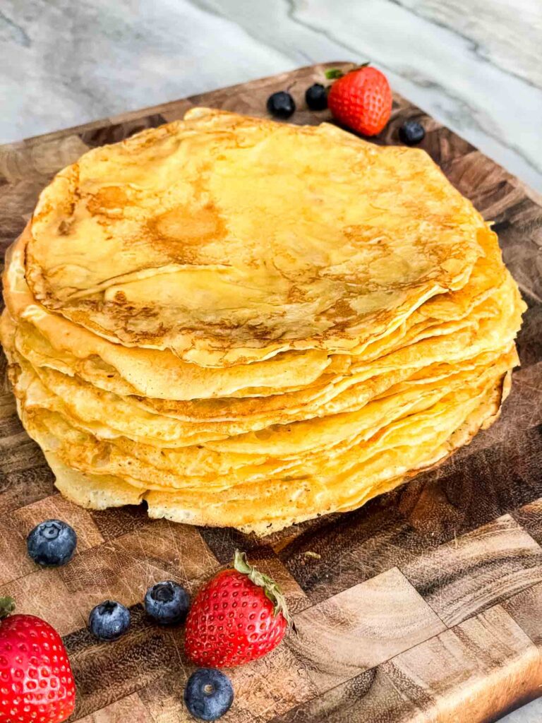A stack of Sweet Crepes on a cutting board surrounded by berries