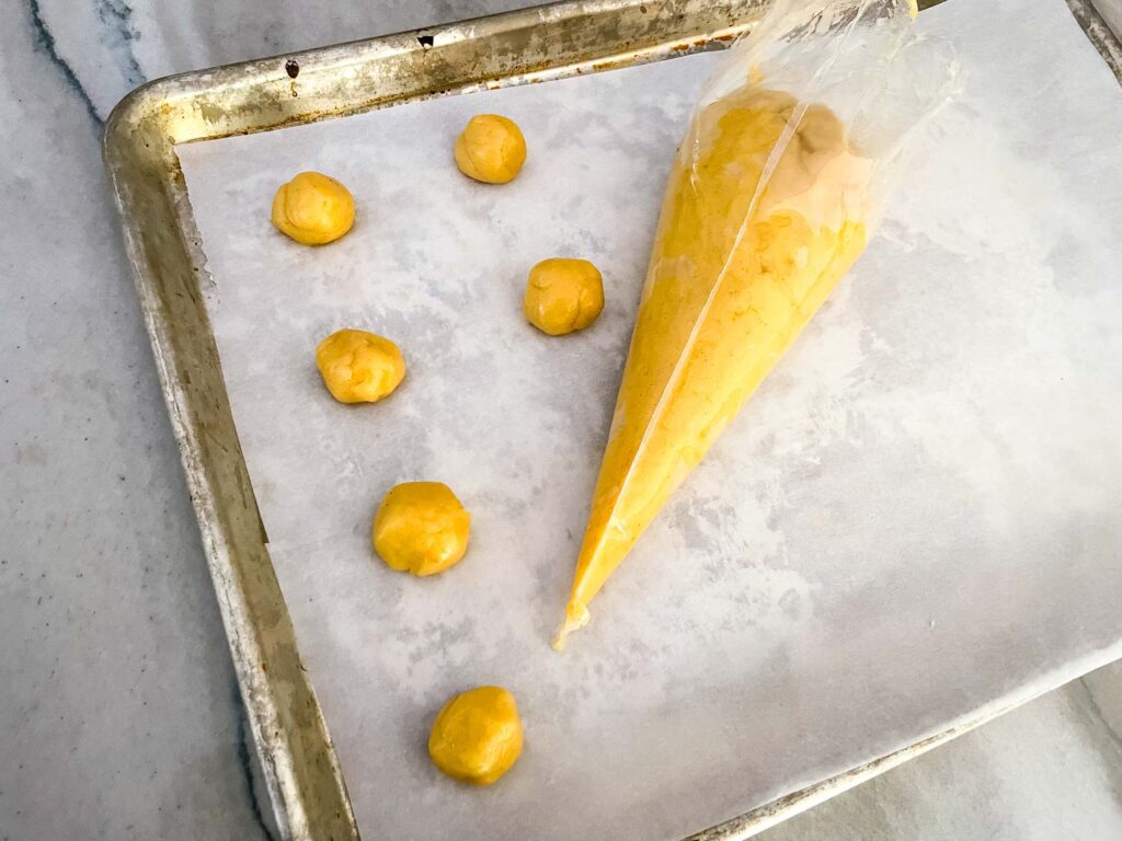 The dough being piped into small balls on a baking sheet