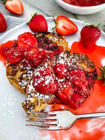 A fork digging into Strawberry French Toast on a white plate
