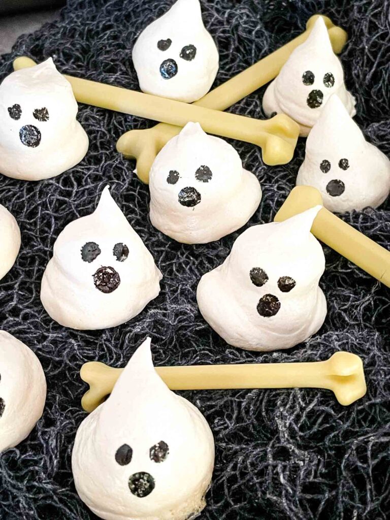 Halloween Ghost Meringues scattered on black cloth with small bones
