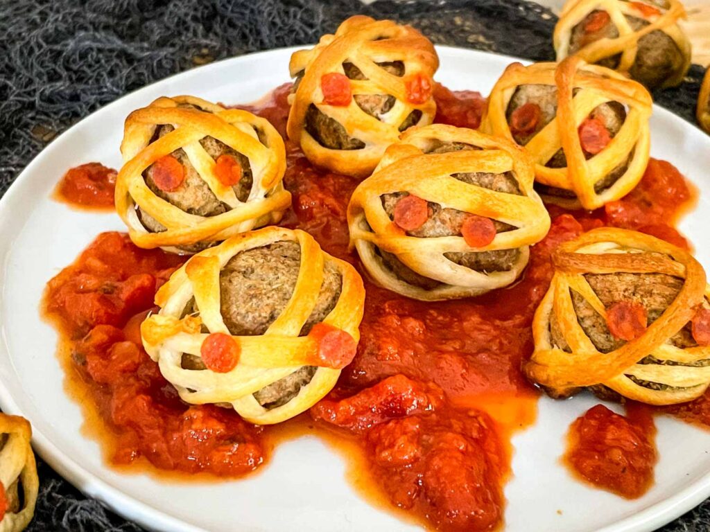Halloween Mummy Meatballs on a bed of marinara on a white plate