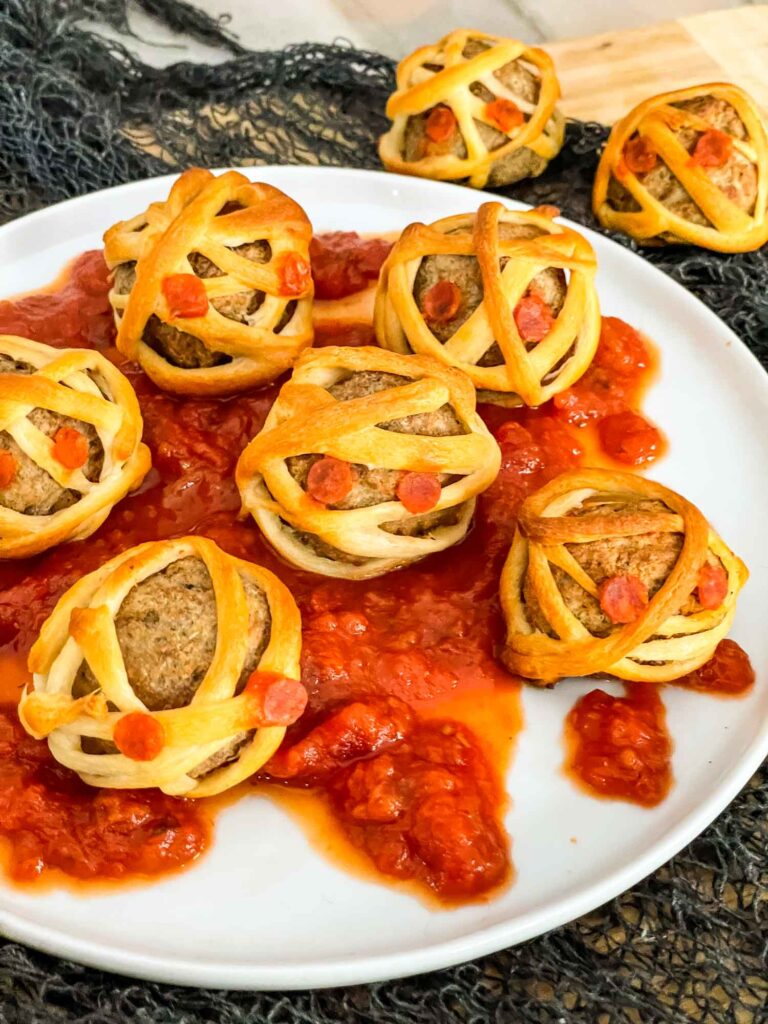 Halloween Mummy Meatballs on marinara sauce on a plate