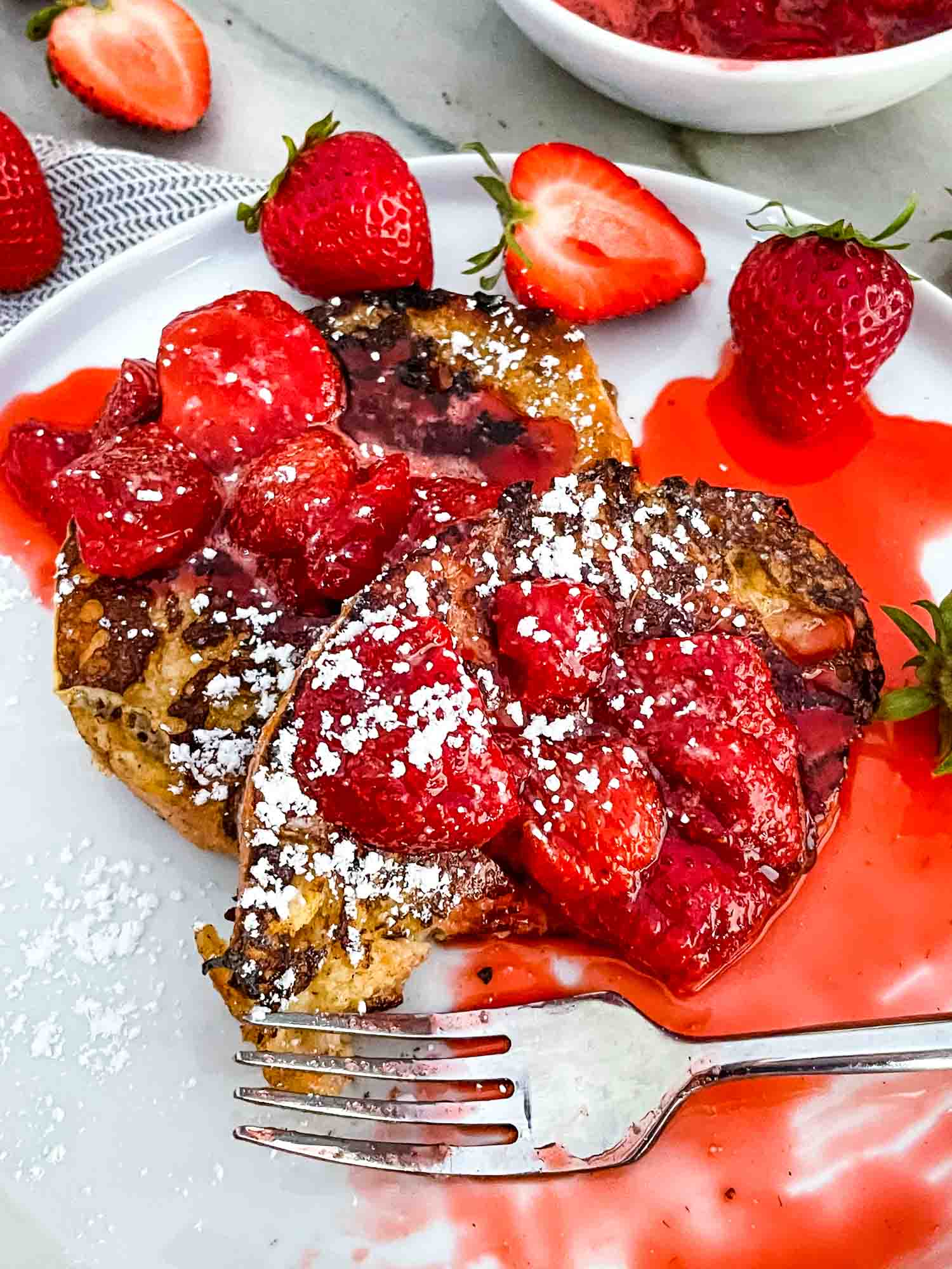 A fork digging into Strawberry French Toast on a white plate