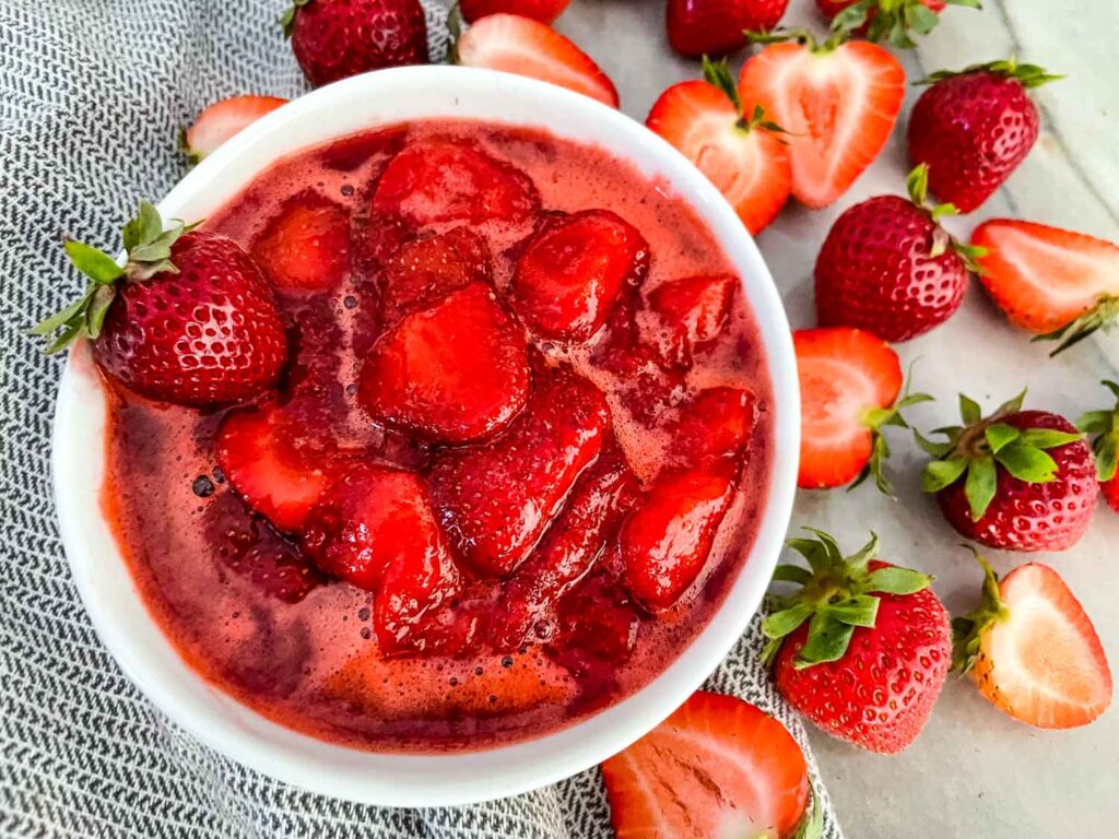 A white bowl of Strawberry Sauce with berries around it
