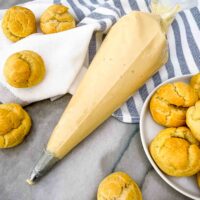 A piping bag full of Vanilla Pastry Cream and surrounded by cream puffs on a blue and white towel