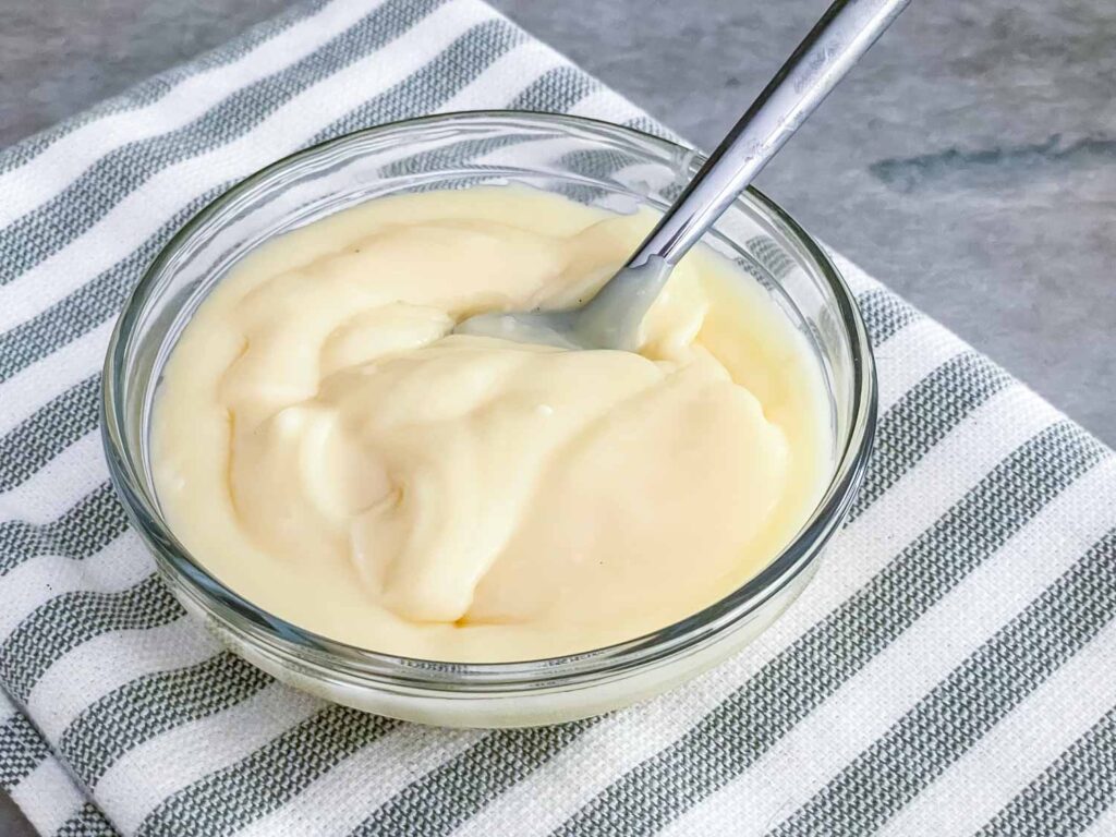 A spoon in a small bowl of White Chocolate Ganache on a striped towel