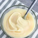 Top view of White Chocolate Ganache in a bowl with a spoon in it, sitting on a striped towel