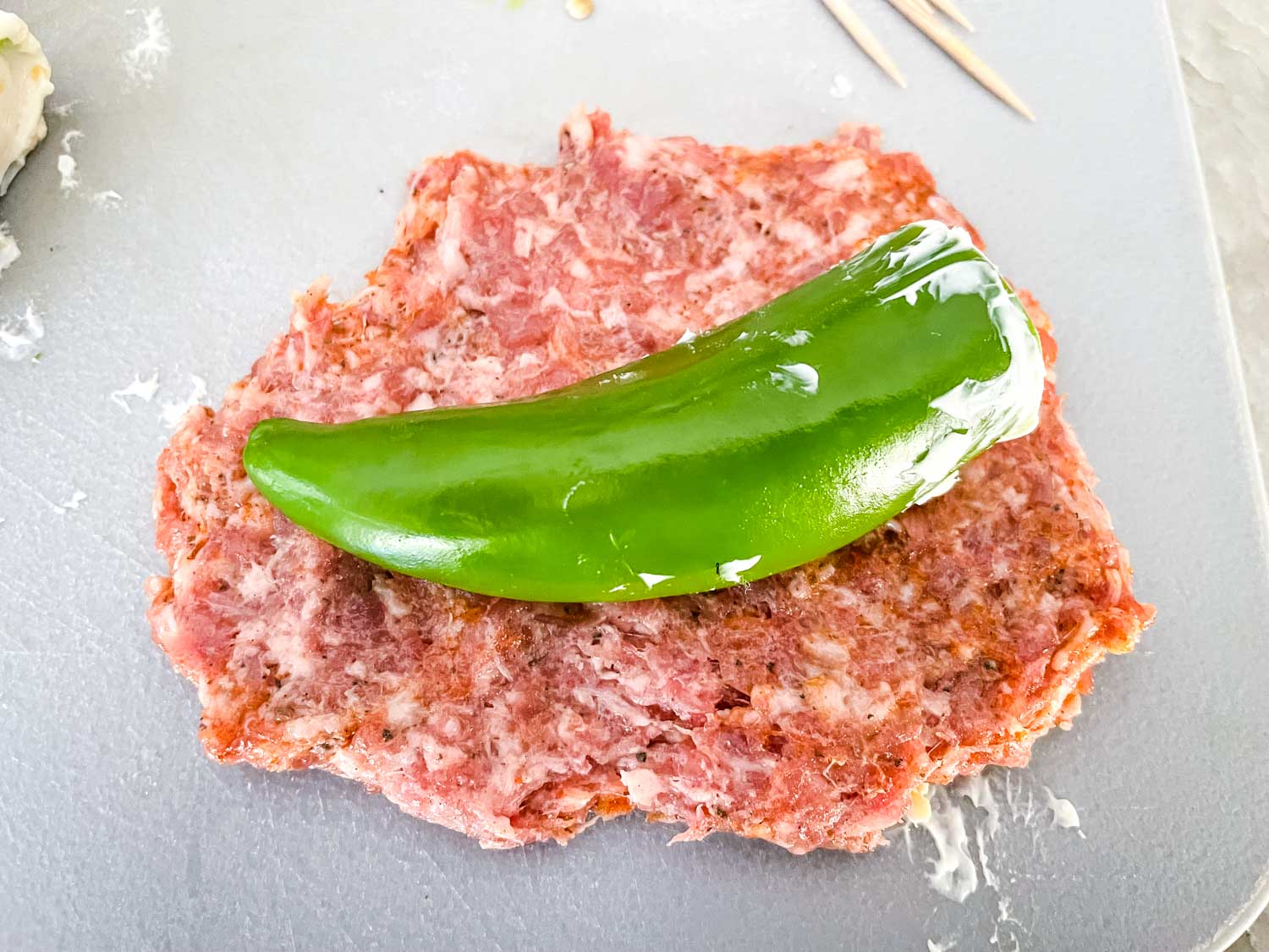 A cheese stuffed pepper sitting on a patty of ground pork