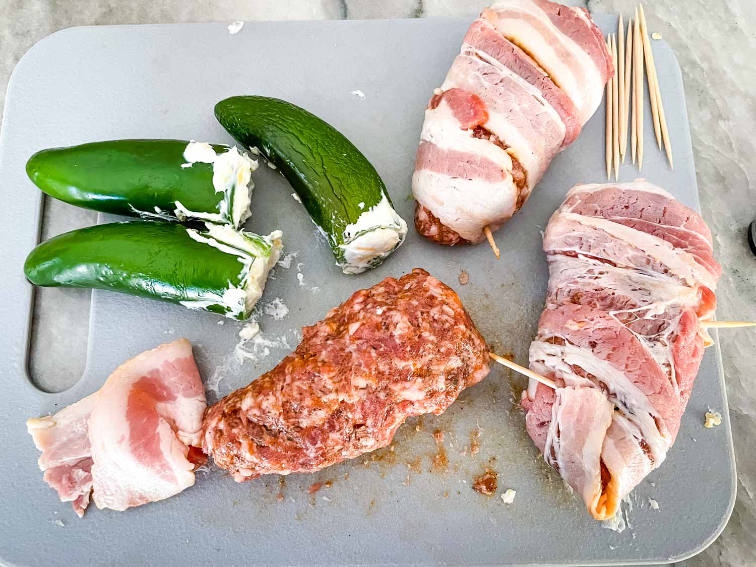 Peppers being filled with cheese, wrapped in pork, and wrapped in bacon