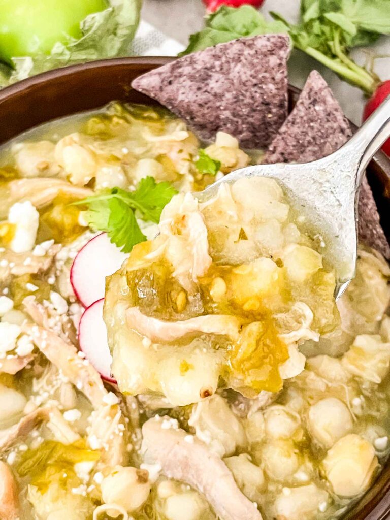 A spoon digging into a bowl of Chicken and Hatch Green Chile Pozole