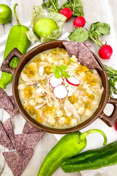 Chicken and Hatch Green Chile Pozole in a brown bowl with topping ingredients around it