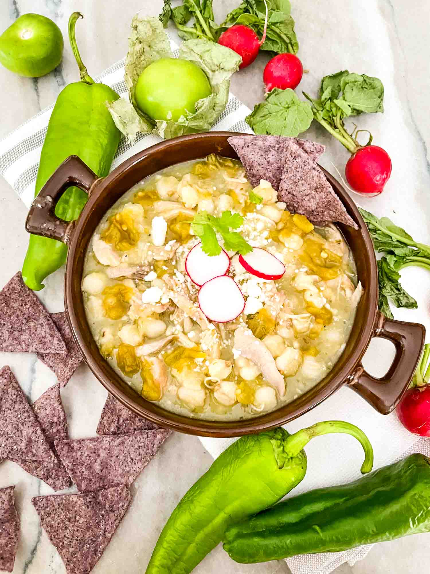 Chicken and Hatch Green Chile Pozole in a brown bowl with topping ingredients around it