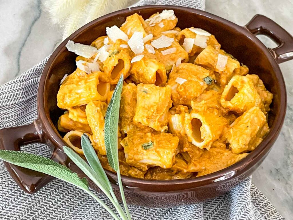 Pumpkin Pasta Sauce in a brown bowl with fresh sage and Parmesan cheese on top