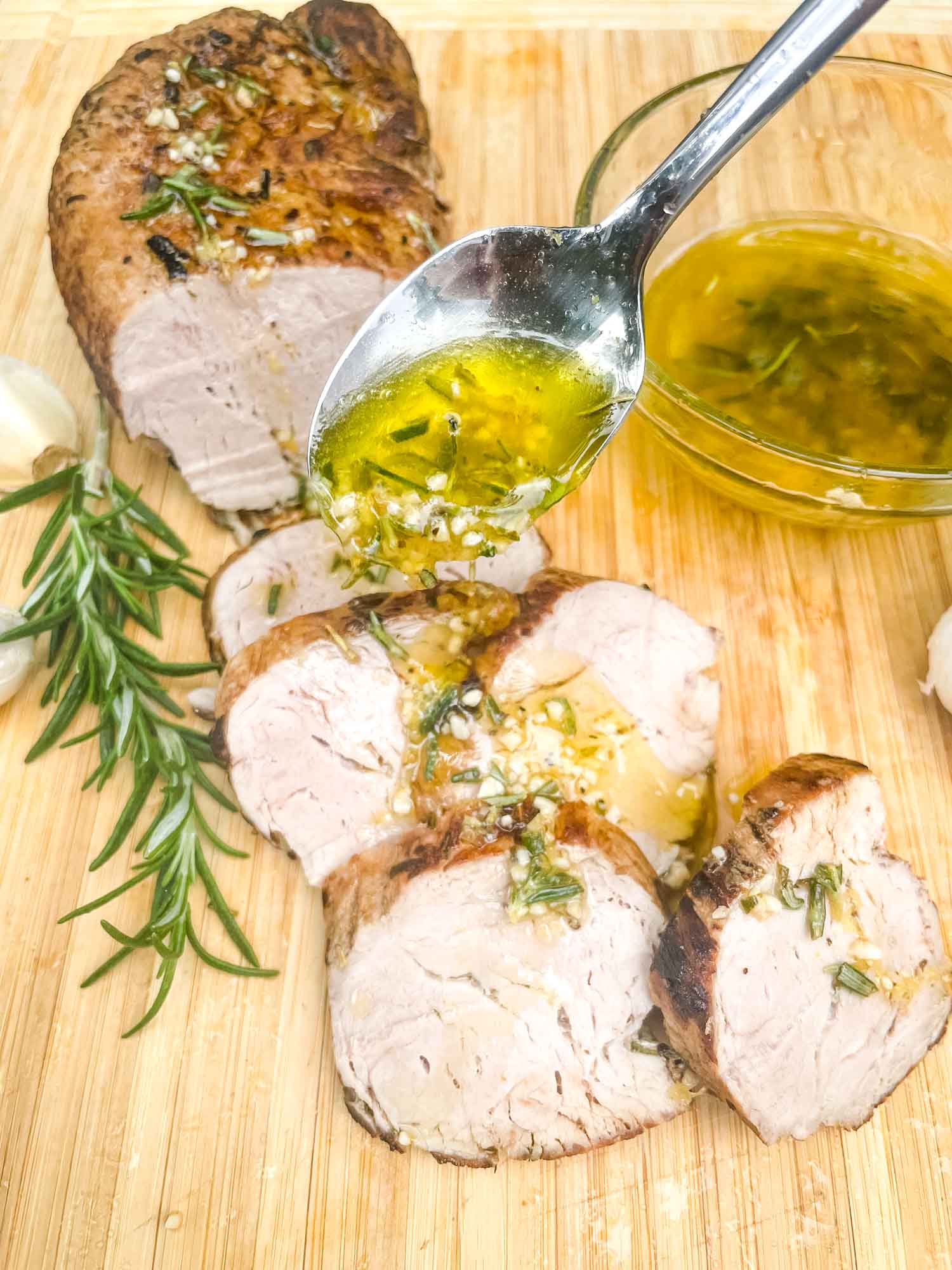 A spoon pouring sauce over sliced Rosemary Garlic Pork Tenderloin