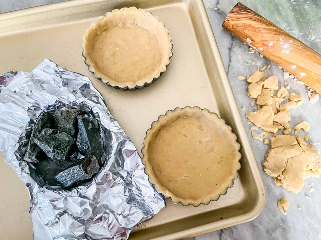 Raw tart crusts being weighed down for baking