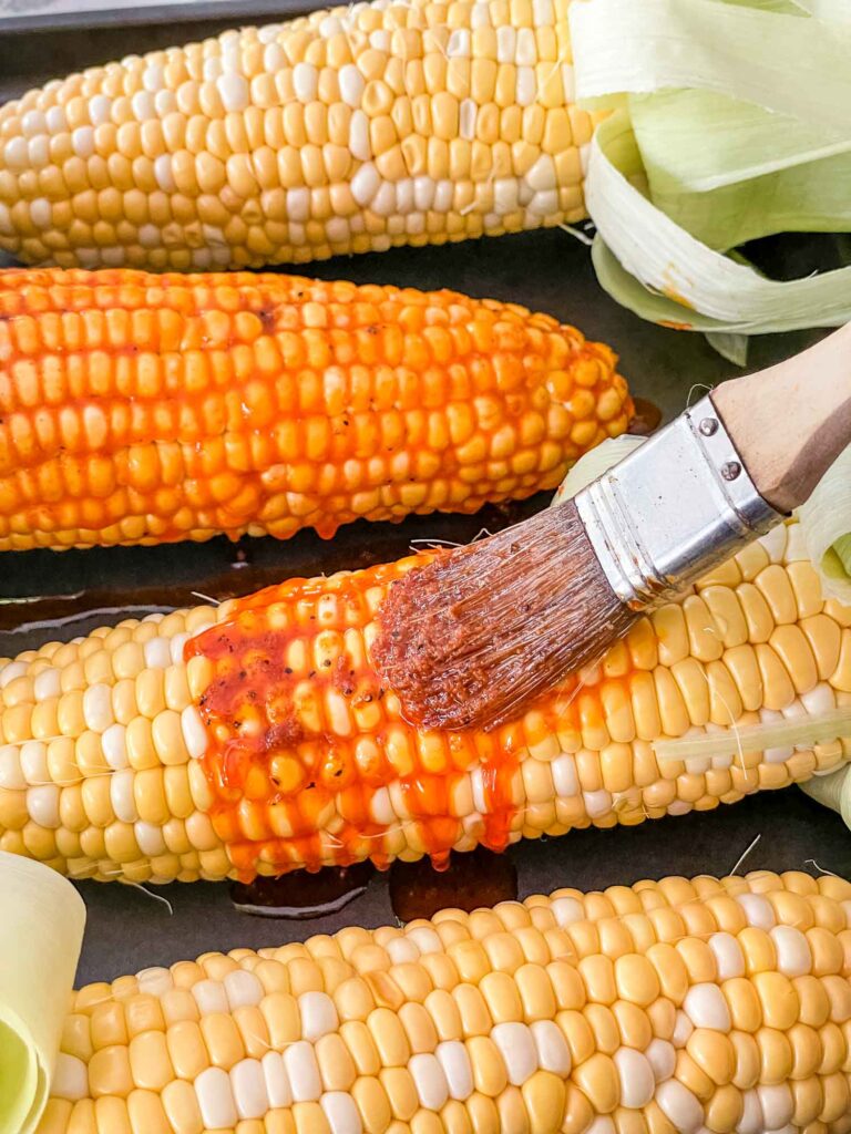 A brush basting the flavored butter onto the corn