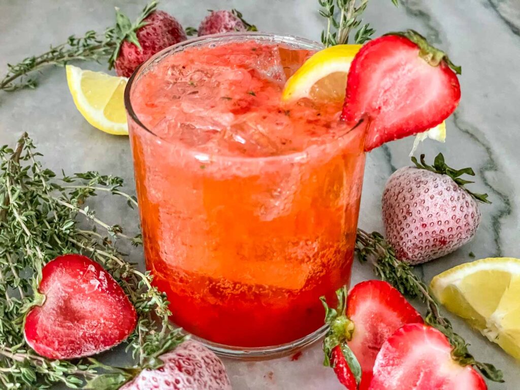A glass of Strawberry Thyme Cooler (Non-Alcoholic Mocktail) with fruit around it