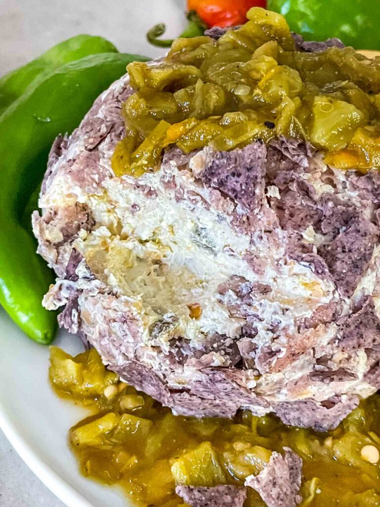 A Hatch Green Chile Cheese Ball with a chunk missing showing the inside mixture