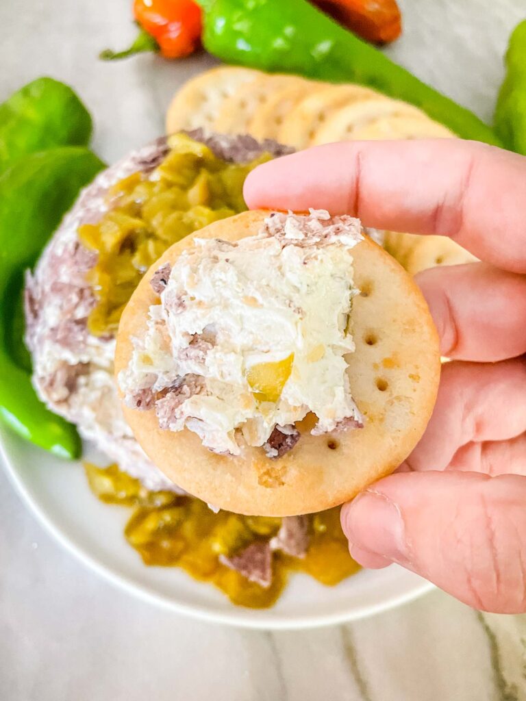 A hand holding a cracker with some of the cheese on it