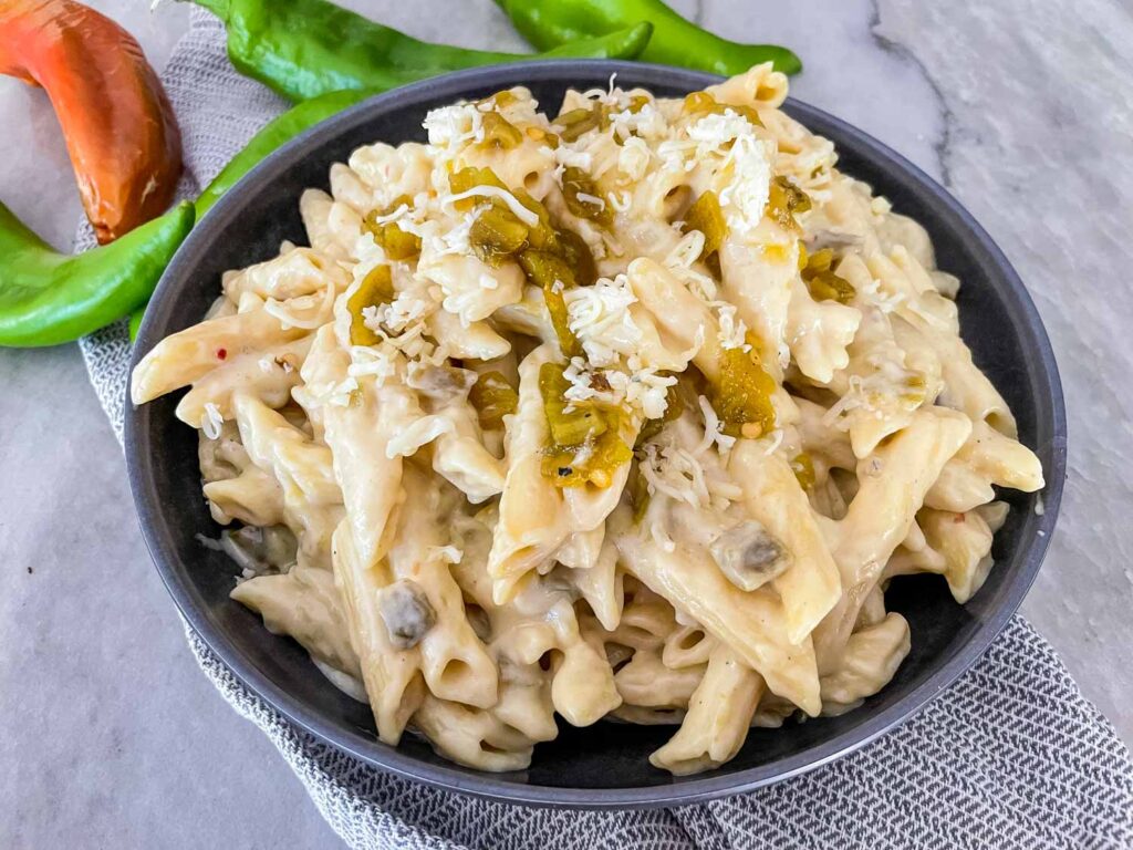 Hatch Green Chile Mac and Cheese piled in a dark bowl on a counter with fresh peppers behind it