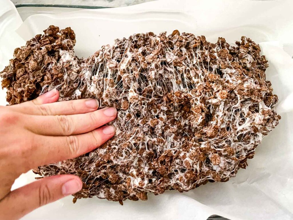 A hand pressing the cereal mixture into a baking dish