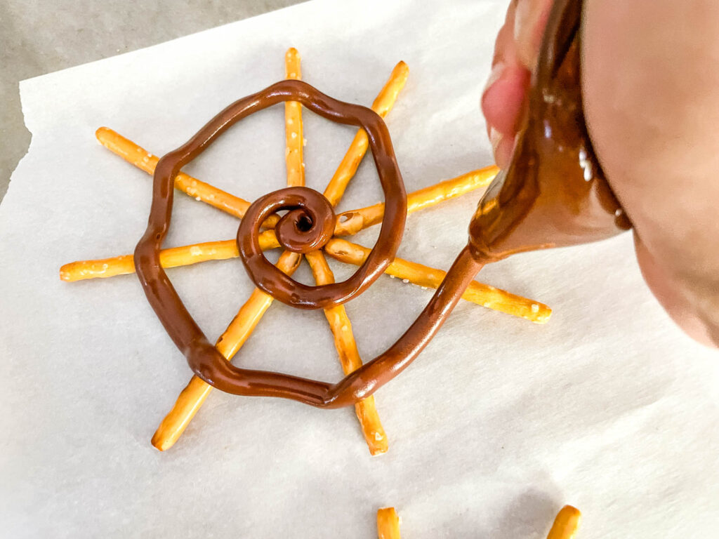 A hand making the chocolate spiral on the pretzels