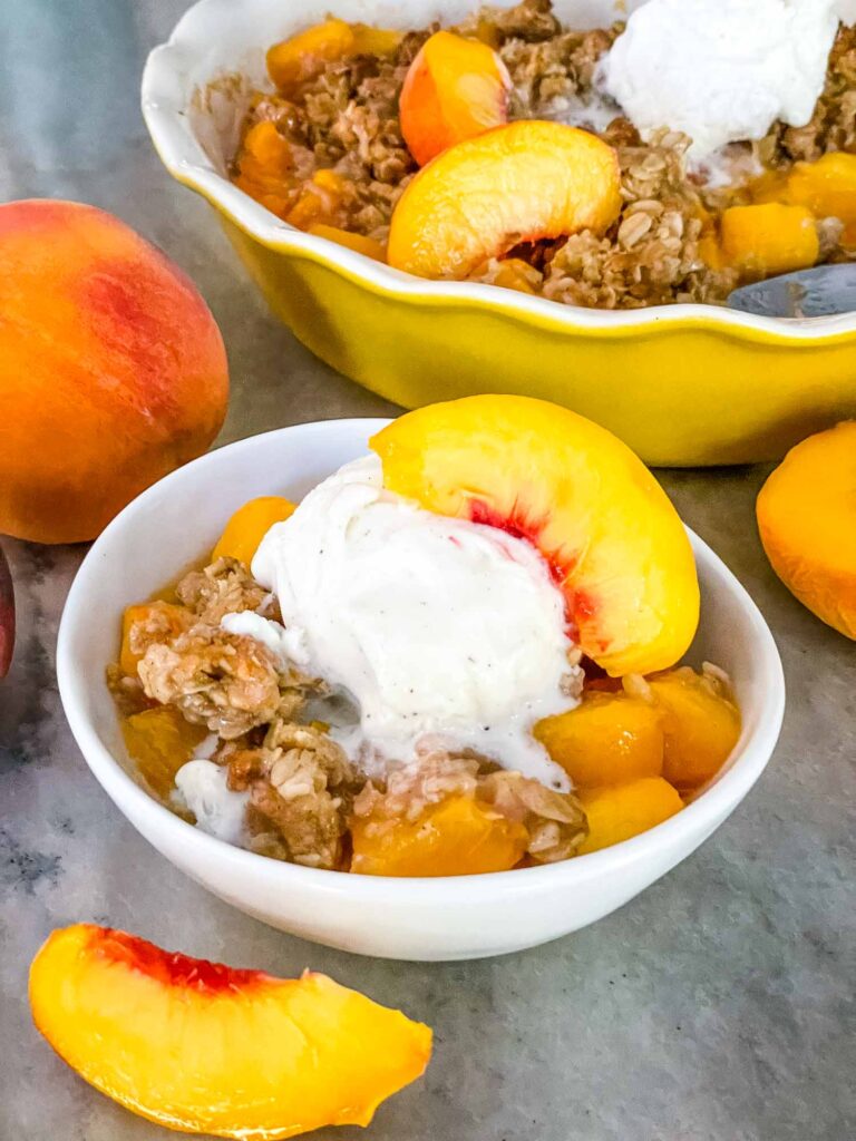 Peach Crisp in a small white bowl with ice crema on top