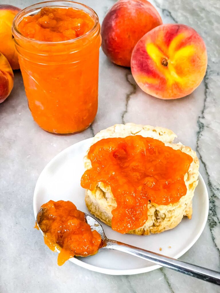 A biscuit with Peach Jam on it and the jar behind it