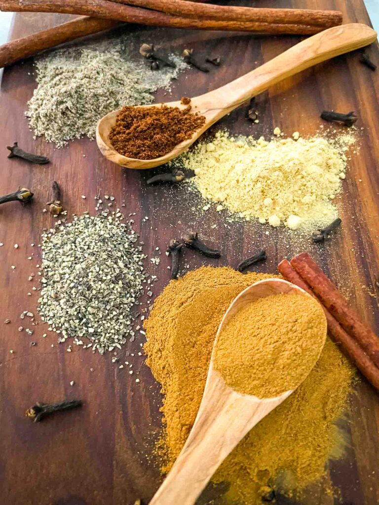 Chai Spices piled on a cutting board with some wooden spoons