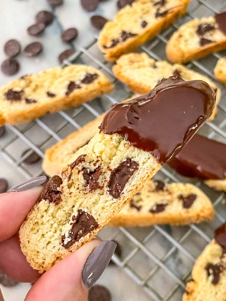 A hand holding a cookie up with more behind it on the counter