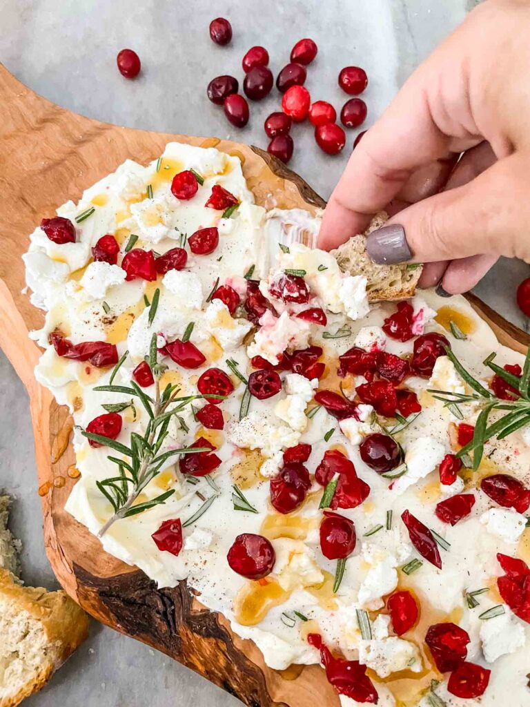 A hand dipping bread into the Cranberry Butter Board