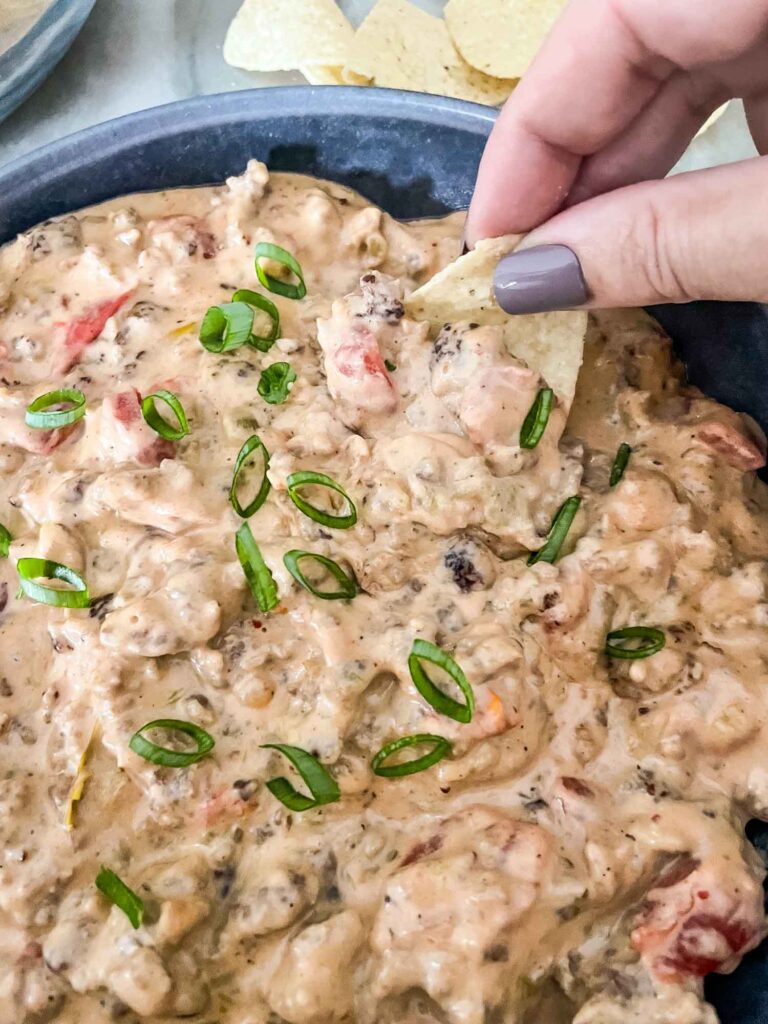 A hand dunking a chip into a bowl of Sausage Dip