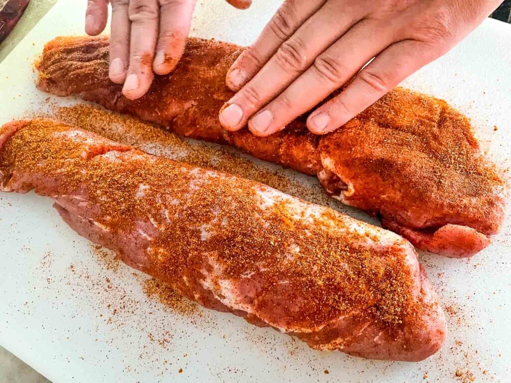 Hands patting the rub onto the meat