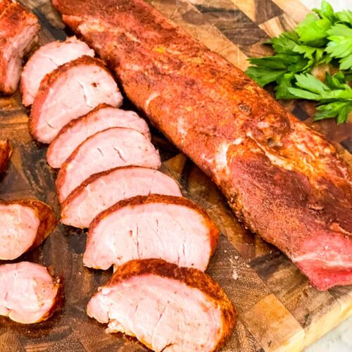 Smoked Pork Tenderloin, one whole and one sliced, on a wood cutting board