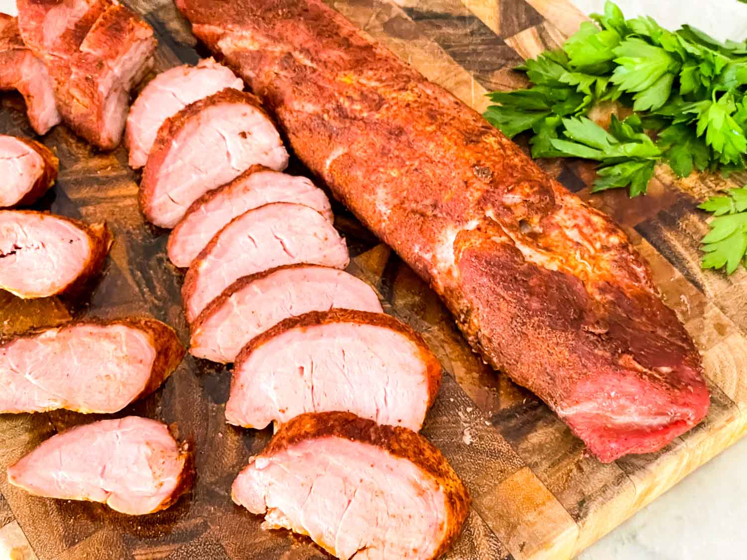 Smoked Pork Tenderloin, one whole and one sliced, on a wood cutting board