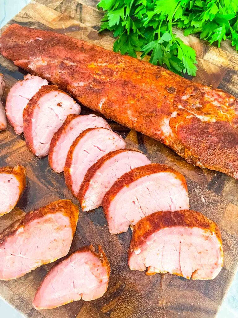 Slices of Smoked Pork Tenderloin next to a whole loin on a cutting board
