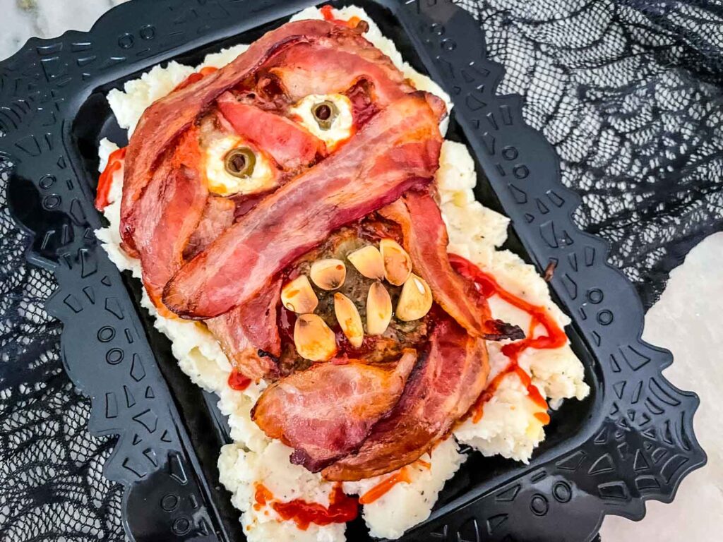 Halloween Mummy Meatloaf on a bed of mashed potatoes on a black platter