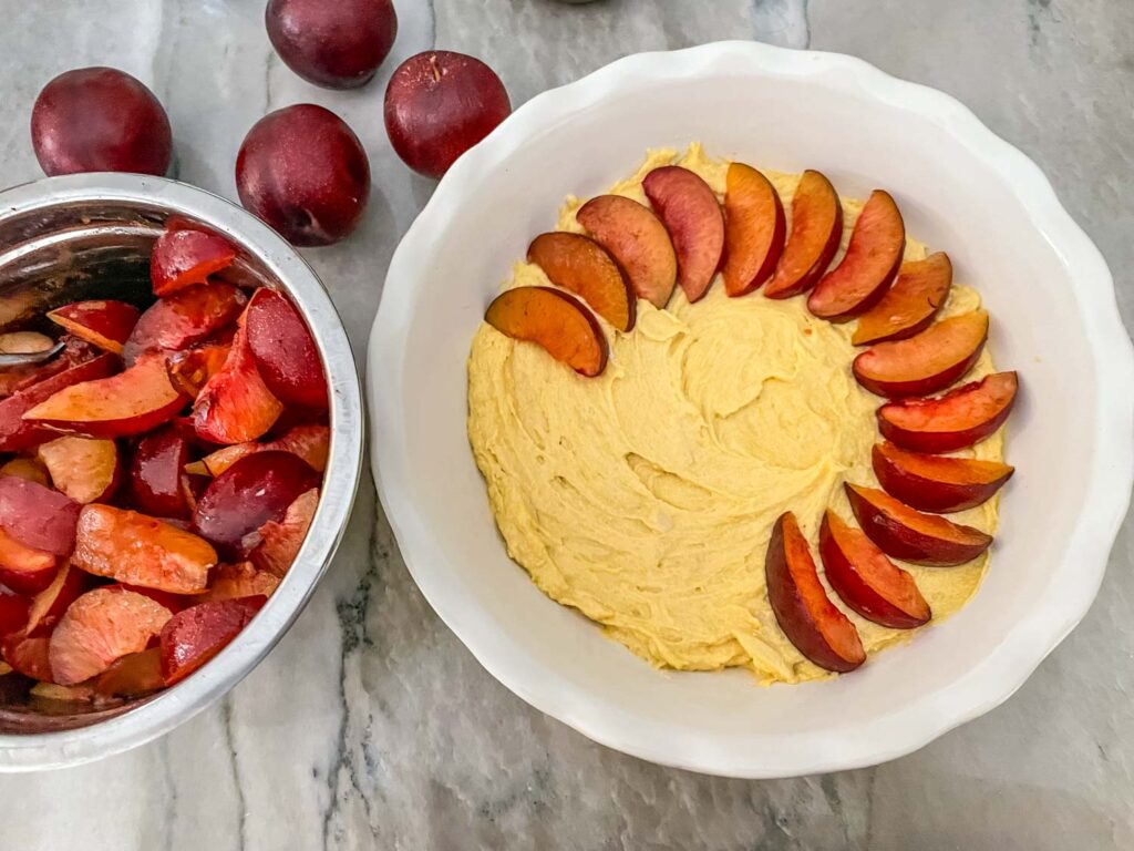 Plums starting to be arranged around the edge of the batter in the pie dish