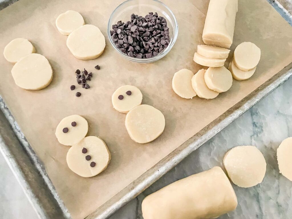 Slicing the dough logs to assemble the snowmen on a cookie sheet