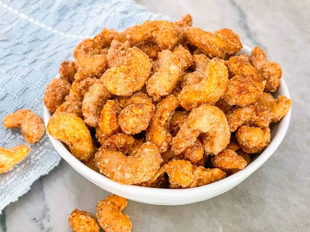 Sweet and Spicy Candied Cashews piled in a small white bowl on a counter