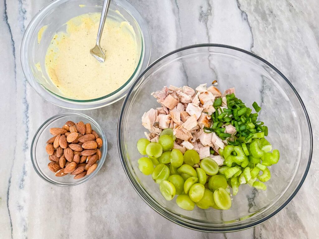 The mixed sauce next to bowls with the nuts and chicken on a counter