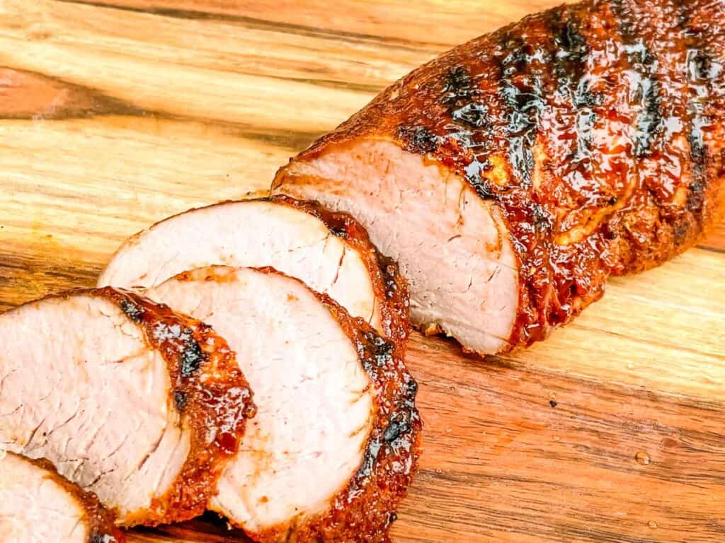 A BBQ Pork Tenderloin partially sliced up on a cutting board