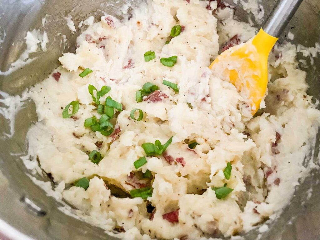 A spoon mixing in the green onions to the mashed potatoes