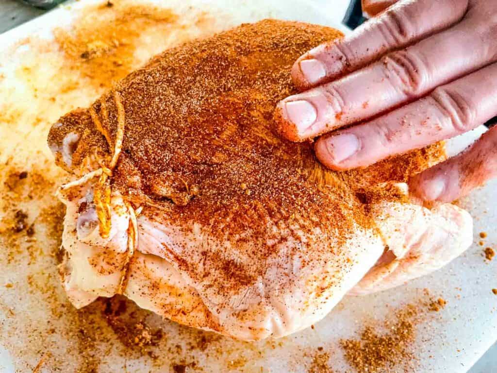 Hands patting dry rub into the chicken