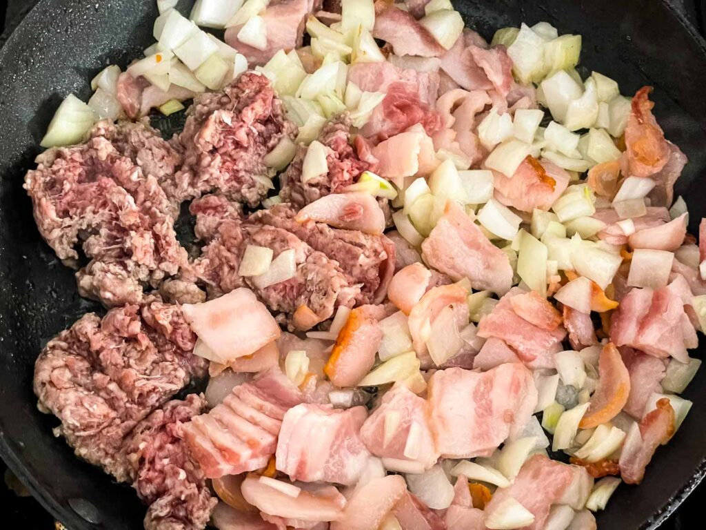 The bacon, beef, and onion cooking in a skillet