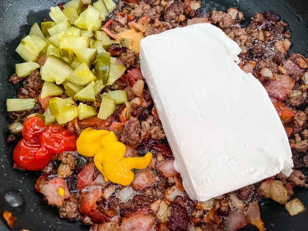 Adding the flavors and cream cheese to the cooked meat in a skillet