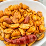 Cajun Spiced Peanuts in a white bowl with a dried red pepper