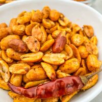 Cajun Spiced Peanuts in a white bowl with a dried red pepper