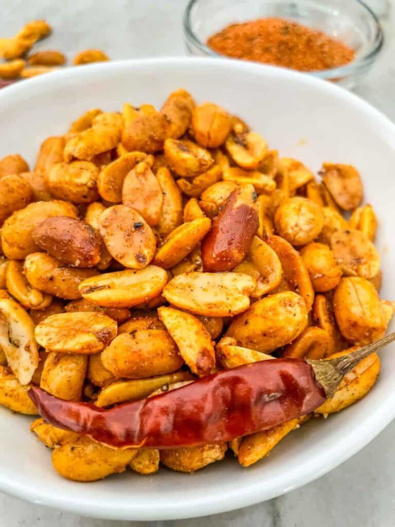 Cajun Spiced Peanuts in a white bowl with a dried red pepper