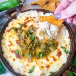 A hand dunking a chip into Hatch Green Chile Cheese Dip